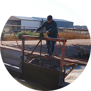 Man standing over an acequia with farmland behind him.